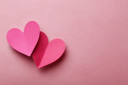 Two overlapping pink paper hearts lie on a textured pink background, symbolizing love and connection on valentine's dayの素材