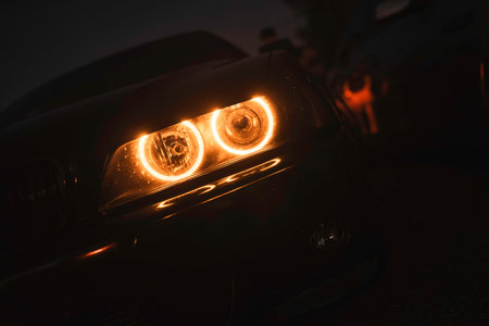 Car headlight is glowing with a warm orange light, illuminating the front of the vehicle in the...