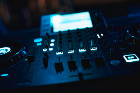 Dj equipment featuring illuminated controls and faders for mixing electronic music at a party,...