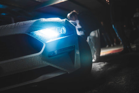 Sports car with a bright led headlight glowing, with water droplets on its surface, standing in a...