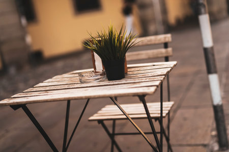 Wooden bistro table and chair sitting empty outside a charming cafe on a street, featuring a small...