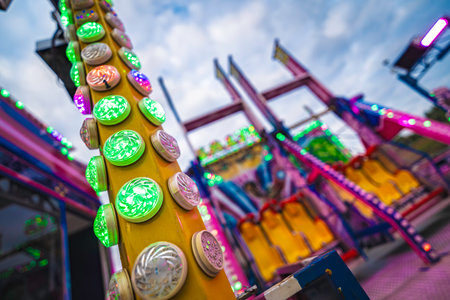 Colorful amusement ride with blinking green and pink lights, motion blur and vivid glow creating energetic, fast-moving carnival atmosphere at an evening fairの写真素材