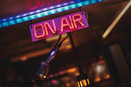 On air neon sign glowing over a vintage microphone in a dark studio, evoking live radio, podcast recording, broadcast production and retro audio communication energyの写真素材
