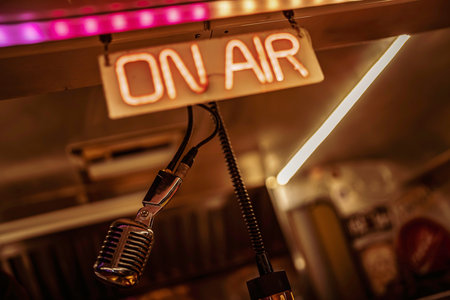 Capturing a retro-style microphone and an illuminated on air neon sign, representing a live broadcast, podcasting, or recording session in a professional studio settingの写真素材