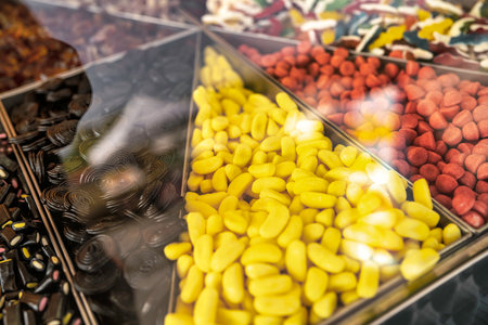 Partitioned bulk candy dispenser filled with colorful treats: yellow banana gummies, red licorice strands and black spiral licorice offering a tempting assortment of sweetsの写真素材