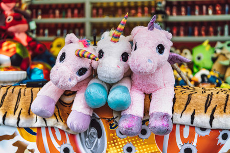 Three colorful unicorn plush toys with rainbow horns sitting on a game stall at a fair, representing fun, childhood, and winning prizes from skill gamesの写真素材