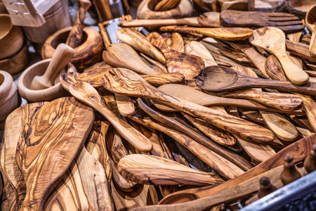 Handcrafted olive wood kitchenware, including various spoons, spatulas, and cutting boards, filling a stall at a vibrant market, showcasing natural patterns and texturesの写真素材