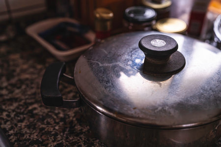 Stainless steel pot with lid closed on speckled kitchen countertop, ready for cooking or keeping a home-cooked meal warm; close-up of everyday cookware and surface textureの写真素材