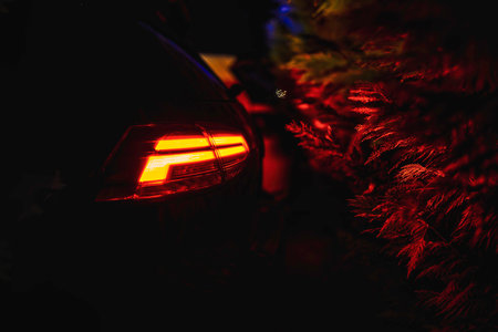 Car taillight illuminating the dark night, creating a strong contrast with reflective red light on...