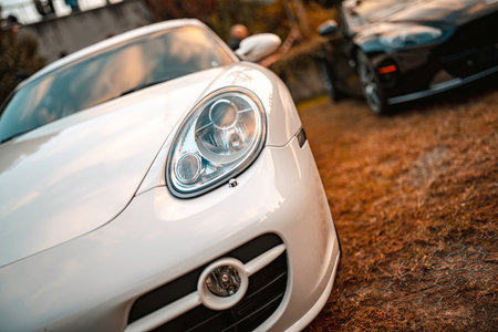 White sports car headlamp reflecting the sky, representing luxury, performance, and modern automotive design, parked outdoors with another dark vehicle in the backgroundの写真素材