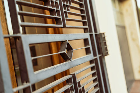 Metal gate bars featuring a repeating diamond and rectangular geometric pattern against a warm, sunlit background, representing security and architectural designの写真素材