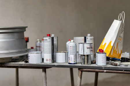 Rovigo, Italy 18 December 2025: workbench cluttered with spray paint cans, paint containers, and a car rim, showing a messy environment for automotive repairのeditorial素材