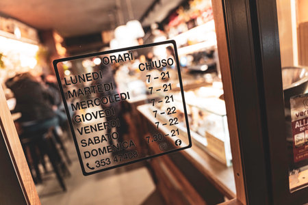 Rovigo, Italy 18 December 2025: Italian patisserie displaying daily opening and closing times on a glass door, offering important information to customersのeditorial素材