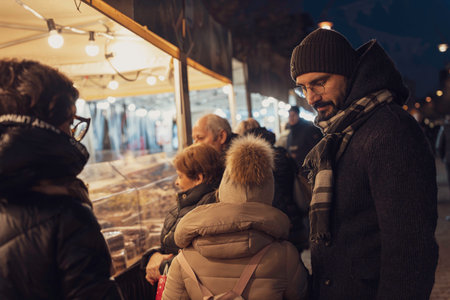 Rovigo, Italy 18 December 2025: family browsing illuminated stall at a bustling night christmas market, enjoying the holiday spirit and togetherness during winterのeditorial素材