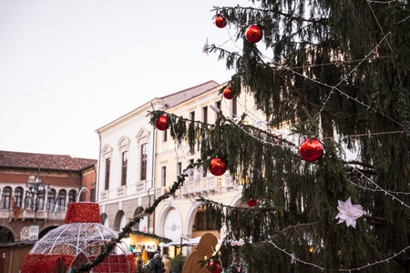 Rovigo, Italy 18 December 2025: christmas tree with red baubles and twinkling lights in historic european town square, festive holiday market atmosphereのeditorial素材