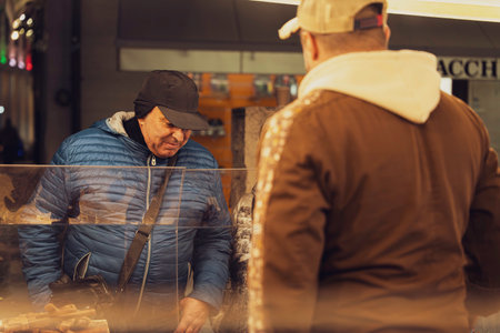 Rovigo, Italy 18 December 2025: customer examines products and chats with vendor at an urban street market stall, candid daily-life shopping and small-business interactionのeditorial素材