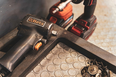 Rovigo, Italy 18 December 2025: pneumatic impact wrench and cordless drill on a grungy metal workbench with assorted screws, nuts and washers in a garage repair settingのeditorial素材