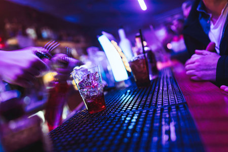 Rovigo, Italy 18 December 2025: bartender preparing a red cocktail with ice and shaking drinks, creating a dynamic scene in the dark, neon-lit bar environmentのeditorial素材