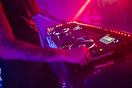 Rovigo, Italy 18 December 2025: dj's hand on a mixer and turntable, mixing vibrant electronic music at a party in a dark nightclub with vivid red and purple lightsのeditorial素材