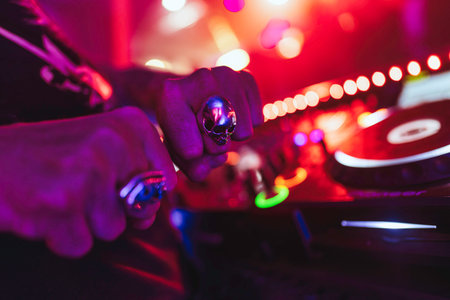 Rovigo, Italy 18 December 2025: dj hands with skull ring on turntable, mixing beats in a vibrant nightclub with red bokeh lights and pulsating energyのeditorial素材
