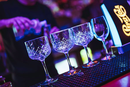 Rovigo, Italy 18 December 2025: bartender preparing cocktails behind a neon purple bar counter with crystal glasses, vibrant bokeh and upscale nightlife vibeのeditorial素材