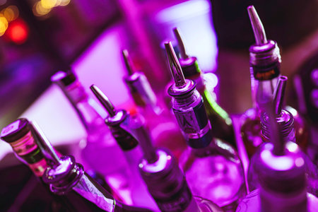 Rovigo, Italy 18 December 2025: bottles of spirits with pourers at a neon-lit bar, purple glow and bokeh creating a moody, modern nightlife cocktail sceneのeditorial素材