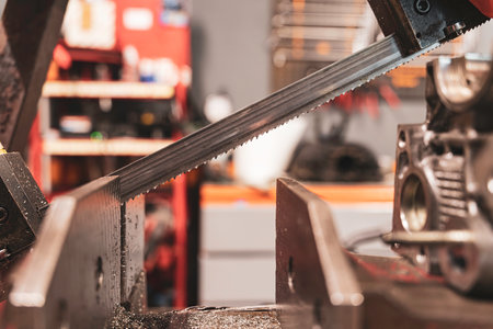 Rovigo, Italy 18 December 2025: bandsaw blade cutting a piece of metal in a busy industrial workshop, creating metal shavings. Fabrication, manufacturing, and industry conceptのeditorial素材