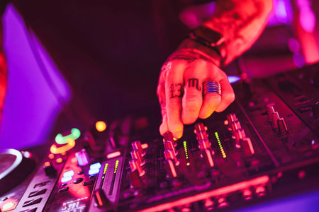 Rovigo, Italy 18 December 2025: tattooed dj hand adjusting mixer faders and knobs, crafting...