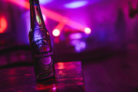 Rovigo, Italy 18 December 2025: heineken bottle on wet wooden bar top, glowing purple and red disco lights with reflective bokeh in a moody nightclub sceneのeditorial素材