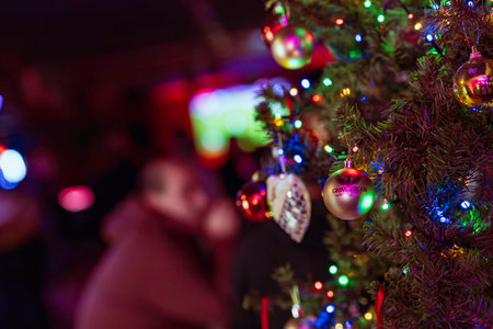 Rovigo, Italy 18 December 2025: Christmas tree decorated with colorful lights and grimbergen branded ornaments, reflecting a vibrant festive atmosphere. People blurred in the backgroundのeditorial素材