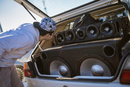 Imola, italy 01 january 2026: man inspecting custom car audio installation in open trunk with...