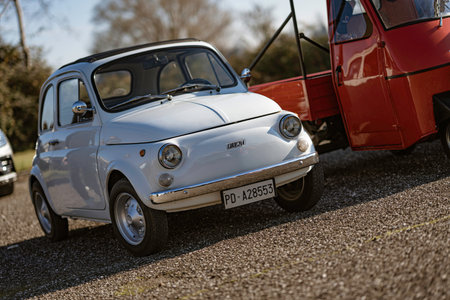 Imola, italy 01 january 2026: fiat 500 vintage white microcar parked beside a red piaggio ape on sunny gravel, classic italian charm and retro travel vibeのeditorial素材