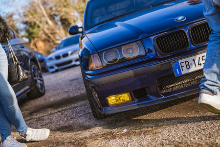 Imola, italy 01 january 2026: blue bmw e36 with yellow fog lights parked at outdoor car meet, people...