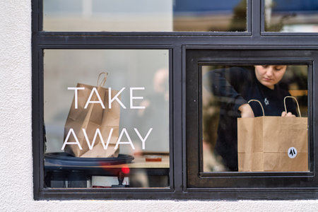 Batumi, georgia 21 april 2026: takeout window service in an urban cafe: worker packs a customer's order into a paper bag through glass with street reflections