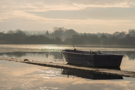 A lone unmanned boat sits idle on a frozen lake during sunrise on Hornsea Mereの写真素材