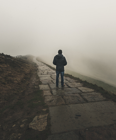A lone figure stands looking into the fog along a pathの写真素材