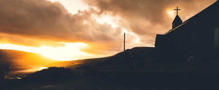 A lone abonded church hides away in the hills alongside a lake in the Peak District, UK during an amazing sunsetの写真素材