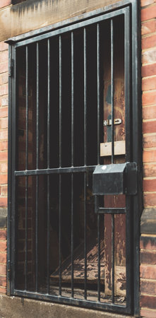 A smashed door behind a black metal gateの写真素材