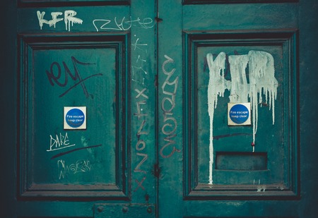 A light blue abandoned fire door with graffiti painted over it.の写真素材