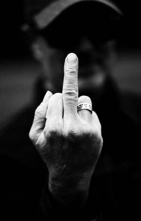 An Angry man sticks up his middle finger at the camera in black and whiteの写真素材