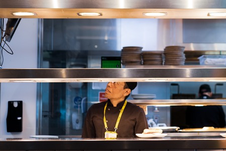 MANCHESTER, UK - 9TH APRIL 2019: A chef in an airport kitchen looks at a screen for the next orderのeditorial素材