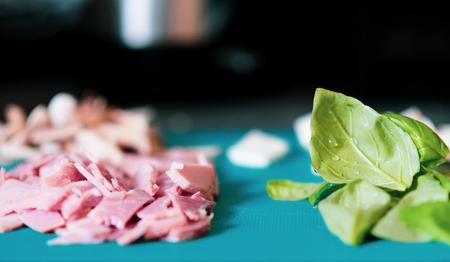 Chopped up ingredients for pizza toppings are laid out on a bright blue chopping board - Includes Basil, Ham, Cheese and mushroomの写真素材