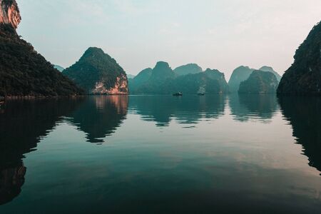 Clear green ember waters reflect the tall limestone islands in Ha Long Bay, Vietnam during a beautiful Sunset with calm, tranquil seas. UNESCO siteの写真素材