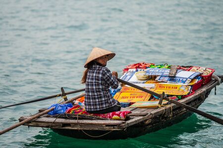 Ha Long Bay, Vietnam - 15th October 2019: A local woman rows up to cruise ships and junk boats with cheap food and beerのeditorial素材
