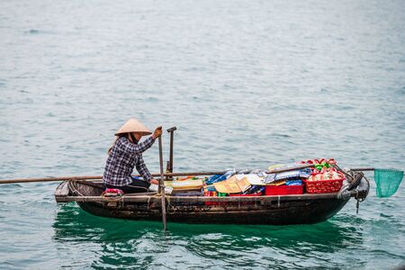 Ha Long Bay, Vietnam - 15th October 2019: A local woman rows up to cruise ships and junk boats with cheap food and beerのeditorial素材