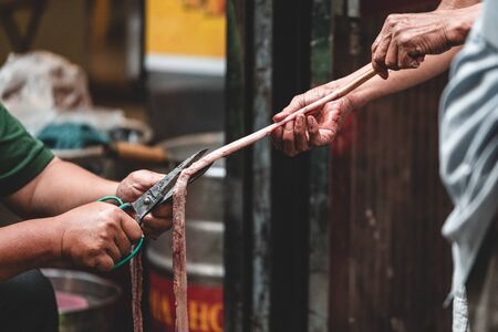 Two Asian men in a back alley cut open intestines or an eel preparing it for a market or street foodの写真素材