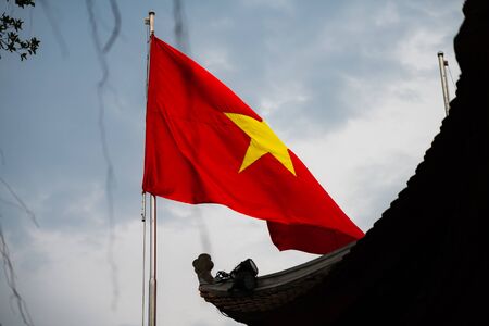 Vietnam Flag waving against a bright blue sky beside a temple in Hanoiの写真素材