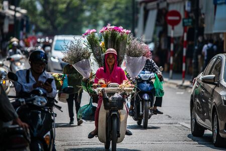 Hanoi, Vietnam - 22nd October 2019: A female courier dressed in pink delivers bunches of flowers using a moped in the captial city of Vietnamのeditorial素材