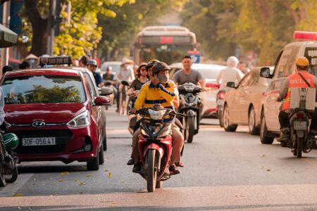 Hanoi, Vietnam - 11th October 2019: A driver and his passenger drive on a moped through the busy streets of Hanoi during sunset driving towards the cameraのeditorial素材