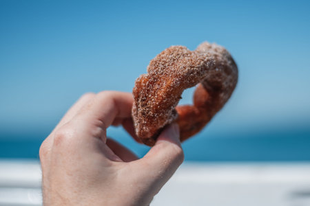 Mini sugary donut held in mans hand with bright blue sky in the background